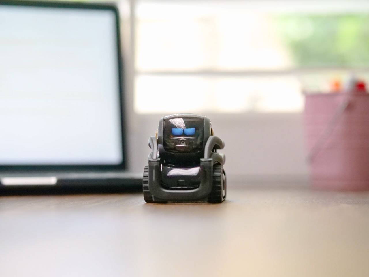 Services Small toy robot on a desk beside a laptop, symbolizing technology and innovation.