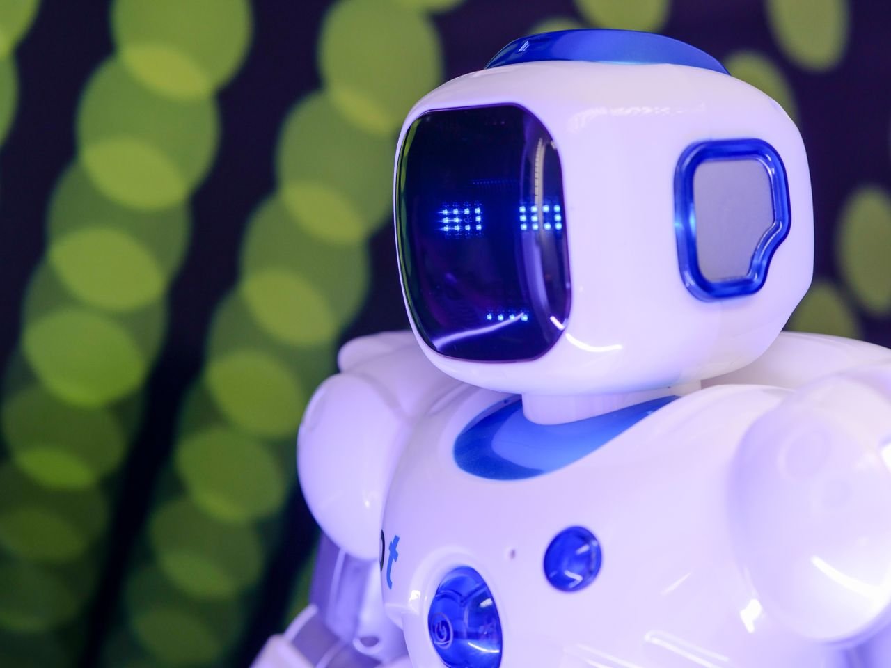 Services Close-up of a modern humanoid robot with glowing blue features on a green abstract background.
